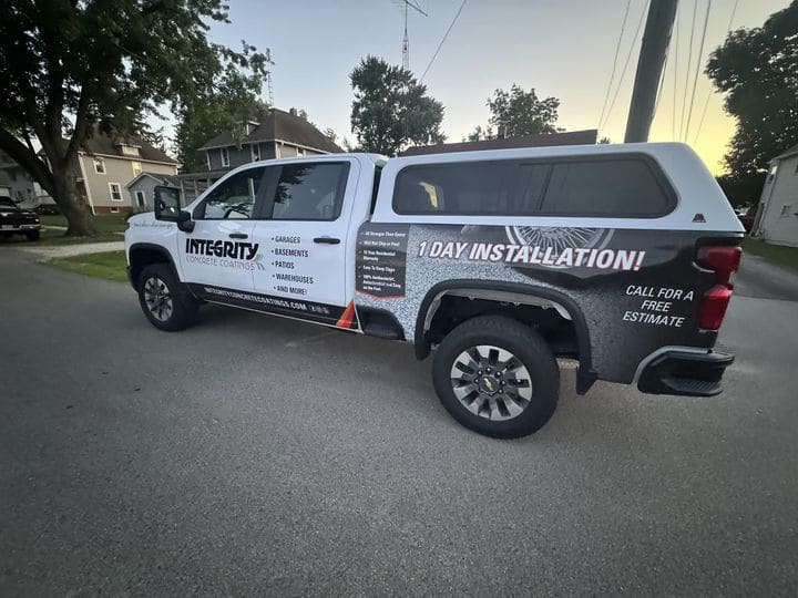 A truck with "Integrity Concrete Coatings" advertisement is parked on a residential street with houses and trees visible in the background.