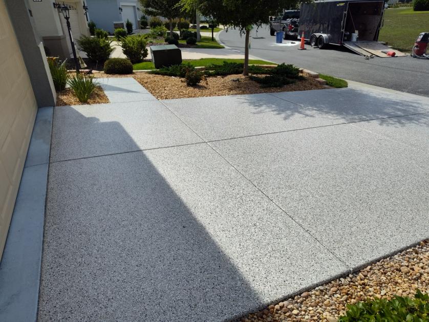 A tidy, freshly paved driveway leads to a suburban home with neat landscaping. A tree and shrubs adorn the front yard; no landmarks identified.