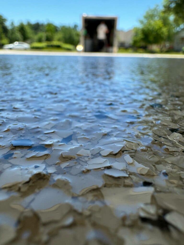 A close-up of a wet surface with a blurred person and green foliage in the background on a sunny day.