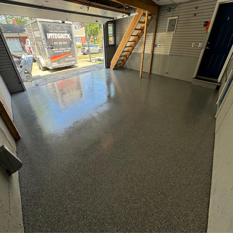 A garage with a newly finished, gray speckled floor. A truck labeled "Integritx Concrete Coatings" is visible outside.