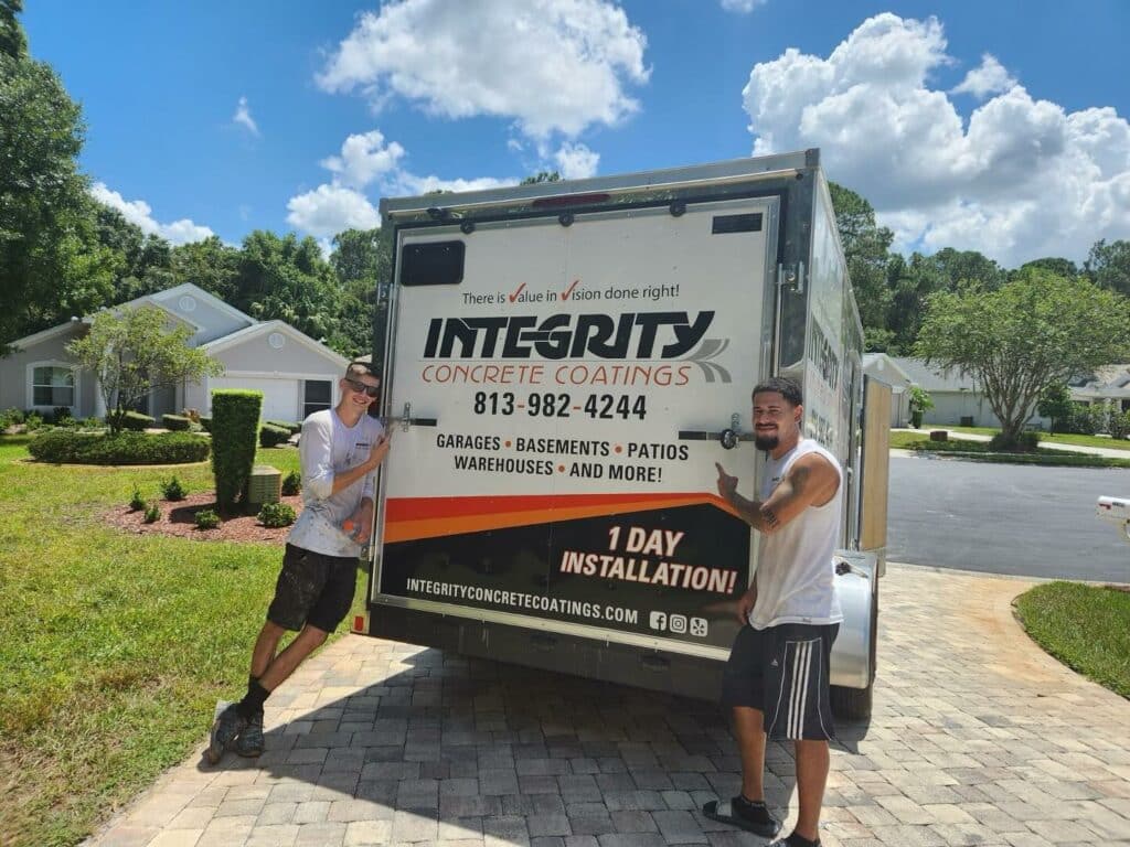 Two people stand beside a truck for Integrity Concrete Coatings in a suburban neighborhood under a clear blue sky.