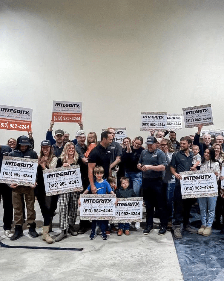 A group of people, including children, holding signs for "Integrity Concrete Coatings" with a contact phone number. They are gathered in a large indoor space.