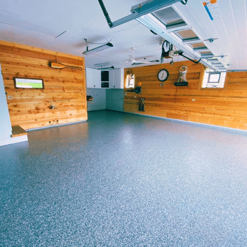 A clean, spacious garage with polished floor, wooden walls, and ceiling fans. Wall clock and decor items are mounted on the walls.