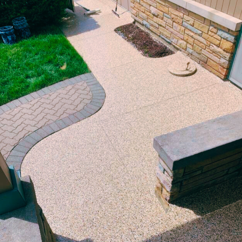 A neatly landscaped garden path with brick edging, surrounded by green grass, leading to a stone and wood exterior wall.