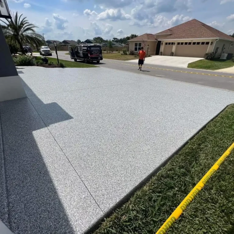 A freshly resurfaced driveway in a residential neighborhood, with a person walking nearby and a truck parked on the street.
