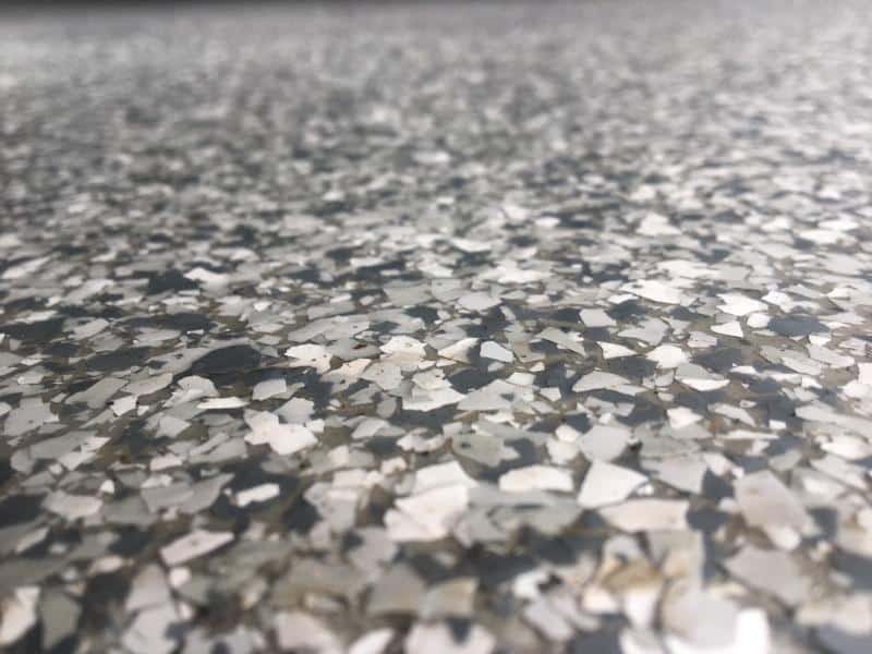 Close-up view of a speckled, textured surface resembling a terrazzo or epoxy floor, featuring gray and white chips with a glossy finish.