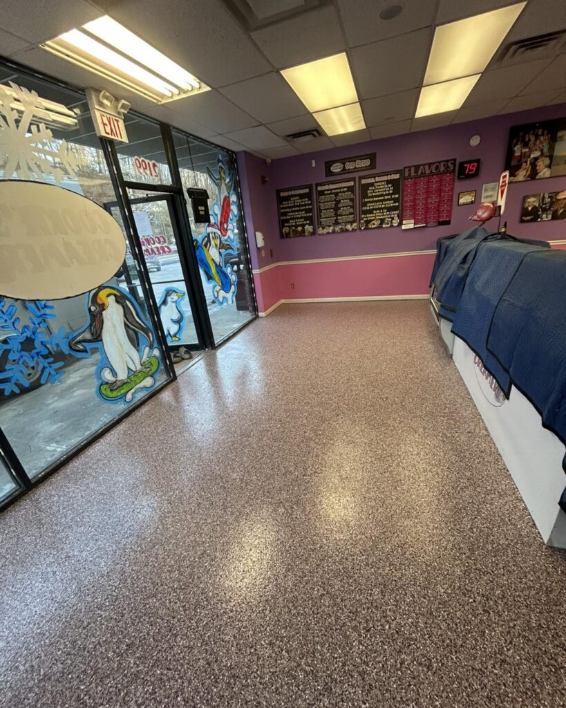 Colorful ice cream shop interior with vibrant wall art and menu displays, featuring penguins and snowflakes on the window. No people visible.